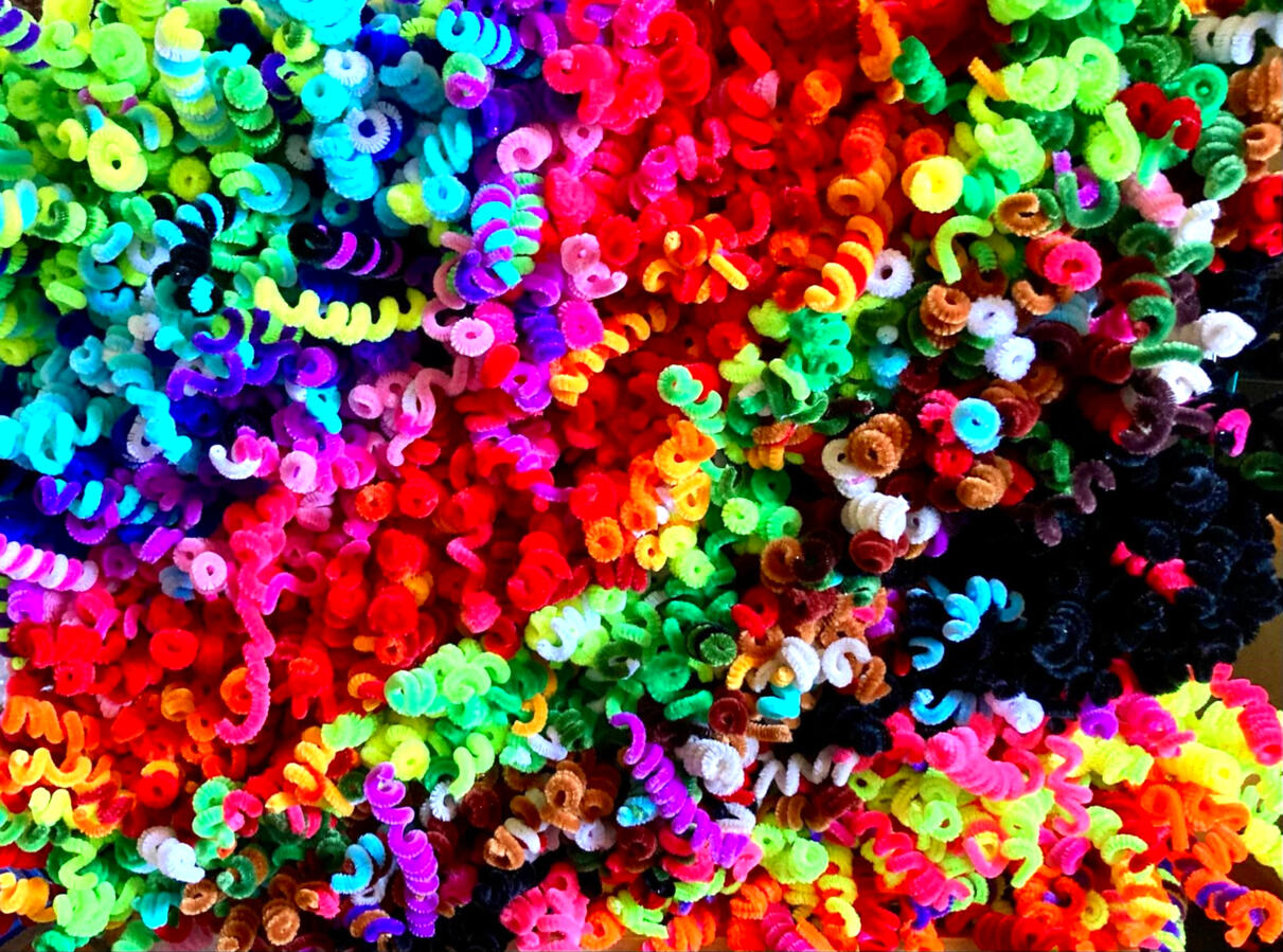 Curly Q about 1500 pipe cleaners all twisted on a pencil and stapled to a canvas board. All sticking off the board. They are made of every color of the rainbow.